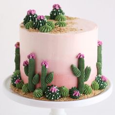 a cake decorated with pink frosting and green cactus decorations on a white pedestal stand