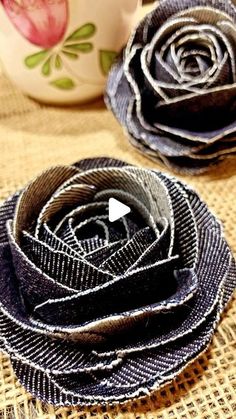 two fabric roses sitting on top of a table next to a coffee cup and saucer