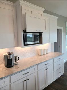 a kitchen with white cabinets and marble counter tops is pictured in this image, there are two coffee mugs on the counter