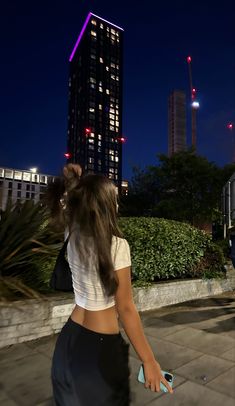 a woman is walking down the sidewalk in front of a tall building at night with her back to the camera