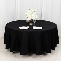 two wine glasses sitting on top of a black table with white flowers in the middle