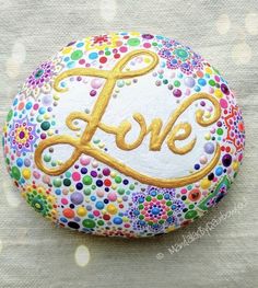 a painted rock with the word love in gold on it's center and surrounded by multicolored dots