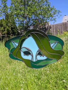 a stained glass sun catcher hanging from a chain in a grassy area with trees and grass