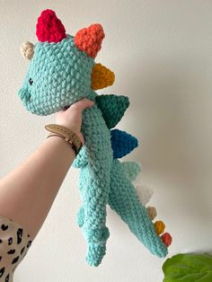 a hand holding a crocheted dragon stuffed animal