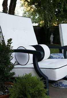 two white chairs sitting next to each other on top of a patio near potted plants