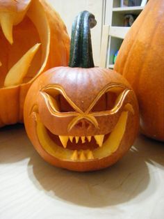 two carved pumpkins with faces and fangs on them sitting on a table next to each other