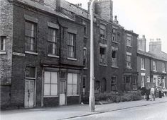 an old black and white photo of people walking down the street in front of brick buildings