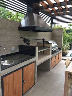 an outdoor kitchen with wood cabinets and stainless steel appliances on the counter top, under a pergolated roof