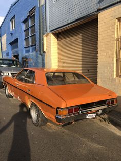 an orange car parked on the side of a street next to a blue brick building