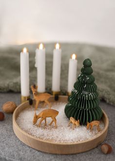 a small christmas tree surrounded by deer figurines in a bowl filled with snow