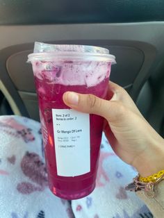 a person holding up a plastic cup with liquid in it on the back seat of a car