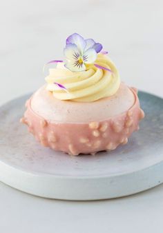 a small cupcake with icing and a flower on top sits on a plate