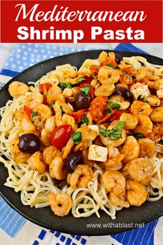 a black plate topped with shrimp pasta and garnished with olives, parsley and tomatoes