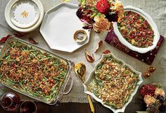 a table topped with dishes filled with green beans and other foods next to glasses of wine