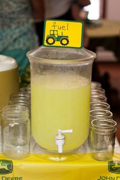 a pitcher filled with liquid sitting on top of a table next to jars and cups