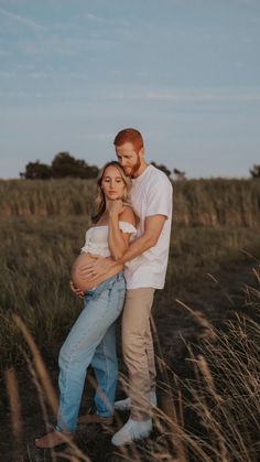 a pregnant couple cuddles in the tall grass at sunset during their photo session