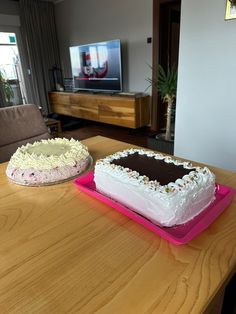 two cakes sitting on top of a wooden table in front of a flat screen tv