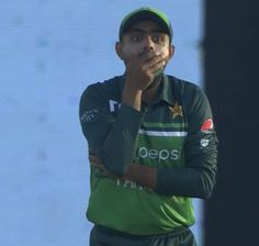 a man standing with his hands on his face while wearing a green shirt and cap