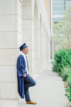 a man in a blue graduation gown leaning against a wall with his feet on the ground