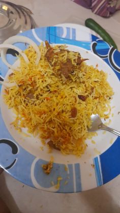 a white plate topped with yellow rice and meat on top of a blue and white table cloth