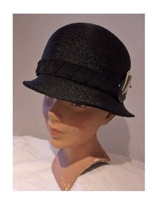 "This cloche hat has all the 1920s style a gal could want. An original 1920s cloche hat, Its in a charcoal black straw, with very Art Deco trims.  A classic cloche, the rounded crown is very deep, coming down over the eyes, with a very brief, downward sloping brim. The black hat band is beautifully folded to create a pattern of geometric chevrons, with a pretty bow at the back; and perched on the left side is a dramatic plastic flourish of a black disc set with a trio of black and white stylised Vintage Black Straw Hat With Short Brim, Vintage Black Brimmed Straw Hat, Adjustable Cloche Hat In Flapper Style, Adjustable Cloche Flapper Hat, Adjustable Black Cloche Hat, Gatsby Style Adjustable Cloche Hat With Curved Brim, Adjustable Gatsby Cloche Hat With Curved Brim, Fitted Flapper Cloche Hat With Brim, Flapper-style Brimmed Cloche Hat For Party