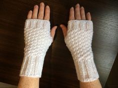 two hands wearing white knitted gloves on top of a wooden table