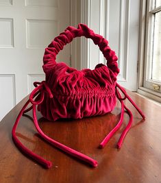 a red purse sitting on top of a wooden table next to a white wall and window