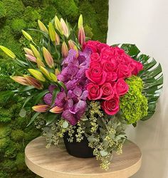 a bouquet of flowers sitting on top of a wooden table next to a moss wall