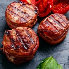 three pieces of meat sitting on top of a table next to tomatoes and green leaves