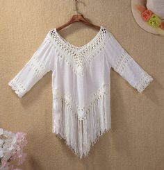 a white blouse with fringes hanging on a hanger next to flowers and a hat