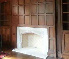 an empty room with wood paneling and a fireplace in the center, surrounded by bookshelves