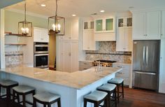 a kitchen with white cabinets and an island in the middle is lit by pendant lights