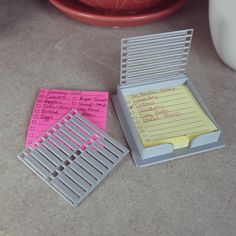 two sticky notes are sitting next to each other on a table with a vase in the background