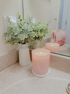 two pink candles sitting on top of a bathroom counter next to a vase with flowers