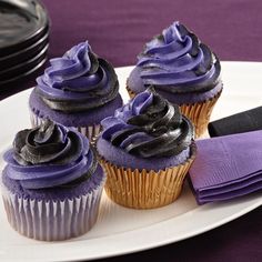 three cupcakes with purple frosting on a white plate next to black plates