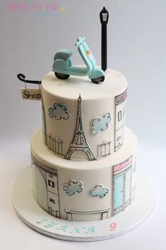 a three tiered cake decorated with the eiffel tower and scooter