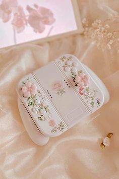 an electronic device with flowers on it sitting on a white bed sheet next to a pink flowered wallpaper