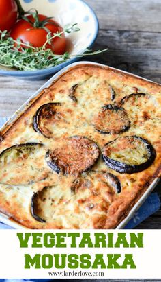 a casserole dish with cheese and vegetables in it on a wooden table next to a bowl of tomatoes