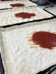 four uncooked pizza doughs with sauce on them