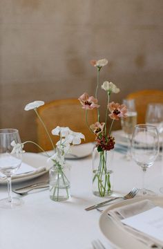 the table is set with white and pink flowers in glass vases on top of it