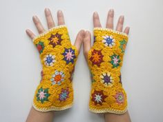 two hands are shown with crocheted flowers on them, and one is wearing a yellow mitt