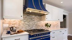 a blue stove top oven sitting inside of a kitchen next to white cabinets and drawers