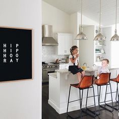 two children sitting on chairs at the kitchen island in front of a black and white sign that says hip hooray