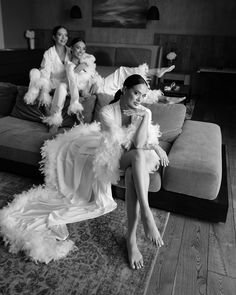 a woman sitting on top of a couch next to two other women in white dresses