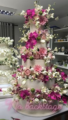 a three tiered wedding cake with pink and white flowers on the top, surrounded by other cakes