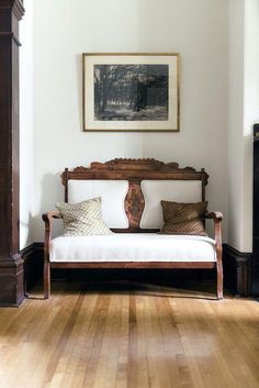 a living room with wood floors and white walls, including a wooden daybed in the corner