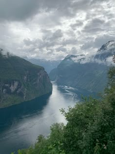 a river flowing through a lush green valley under a cloudy sky with mountains in the background