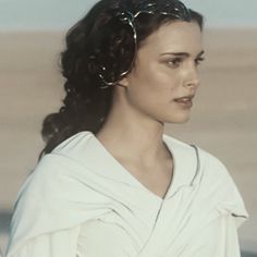 a woman in a white dress is standing on the beach with her hair pulled back