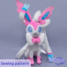 a stuffed animal with blue eyes and pink ears sitting next to another stuffed animal on a gray background