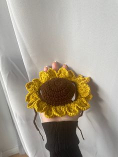 a person is holding up a crocheted sunflower with their hands on the wall